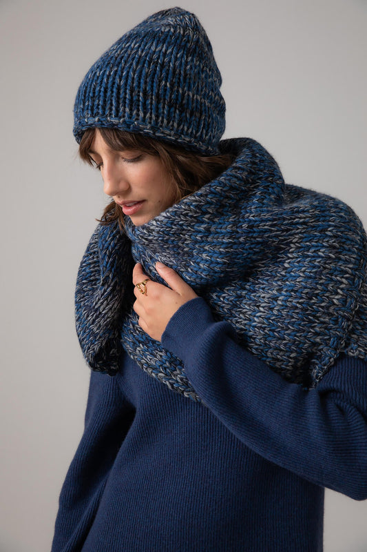Johnstons of Elgin’s Marl Chunky Cashmere Beanie and Square Scarf Giftset in Navy on a model wearing a ombre cashmere cape on a grey background AW23GIFTSET8A